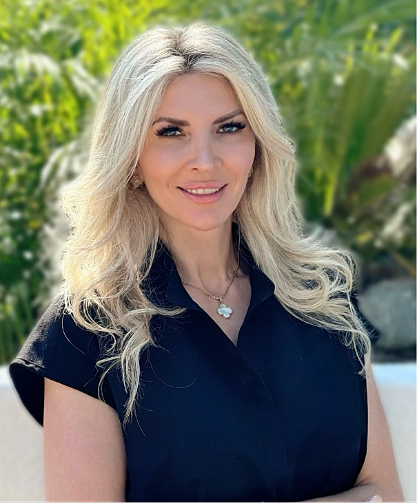 Woman smiling outdoors with lush greenery background.