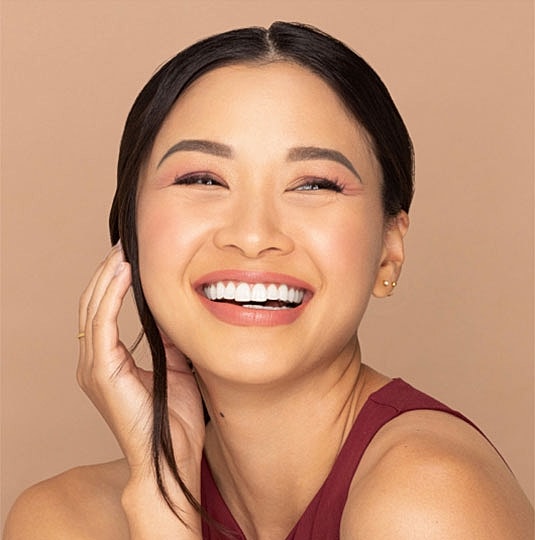 Smiling woman with long hair against beige background.